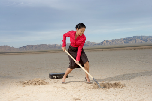 Businesswoman digging hole in dry lake bed