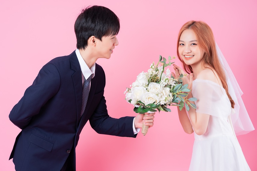 Young Asian bride and groom posing on pink background