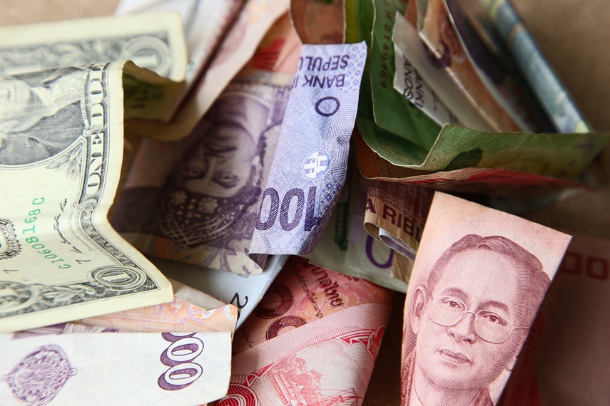 A high angle shot of a pile of banknotes from different countries on a wooden surface